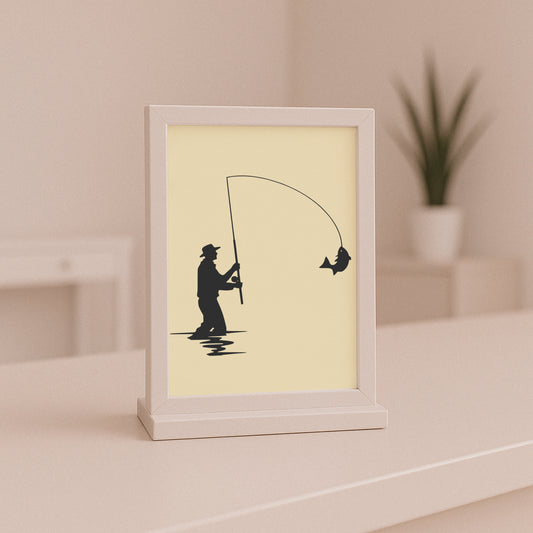 Framed artwork of a black silhouette of a fisherman and fish on a beige background.