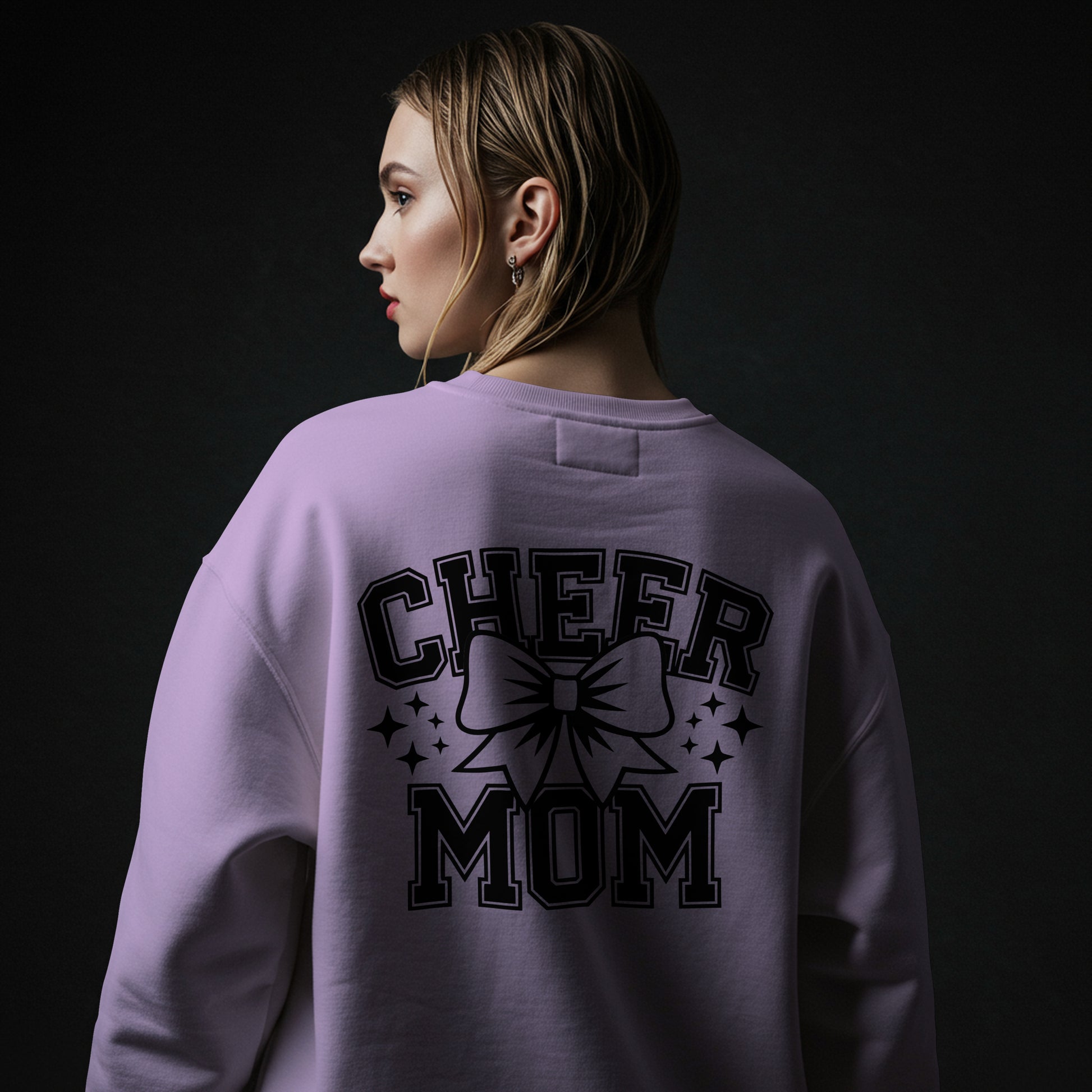 Person wearing a purple sweatshirt with 'CHEER MOM' text and bow graphic on the back against a black background