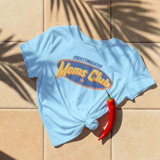 Light blue t-shirt with 'Overstimulated Moms Club' text on a beige surface with a red chili pepper.