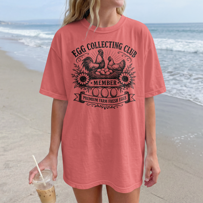 Person wearing a pink t-shirt with 'Egg Collecting Club' design on a beach.
