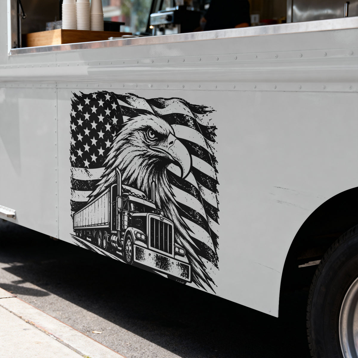 A black and white graphic decal on the side of a white food truck, featuring an eagle head, American flag, mountains, pine trees, and a semi-truck.