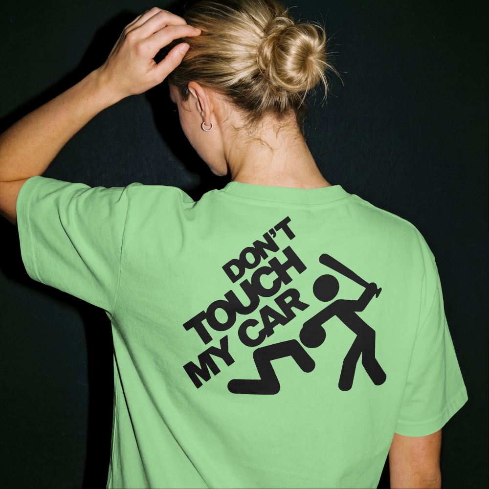 Person wearing a green t-shirt with 'Don't Touch My Car!' text on the back against a black background