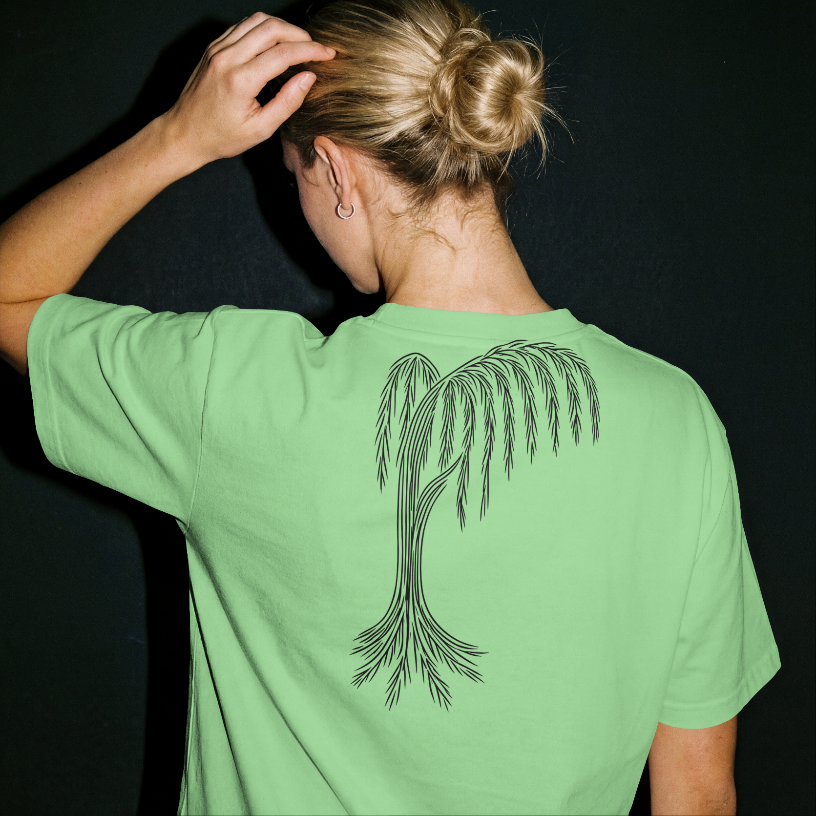 Person wearing a green t-shirt with a palm tree design on the back against a black background
