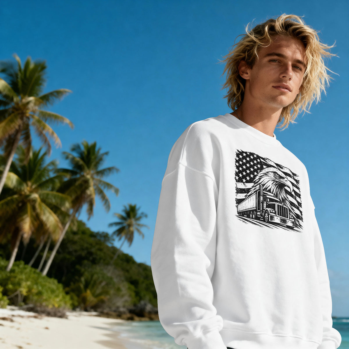 A blonde man wearing a white crewneck sweatshirt with a black graphic print of a cabin under an American flag, standing on a tropical beach with palm trees and blue sky.