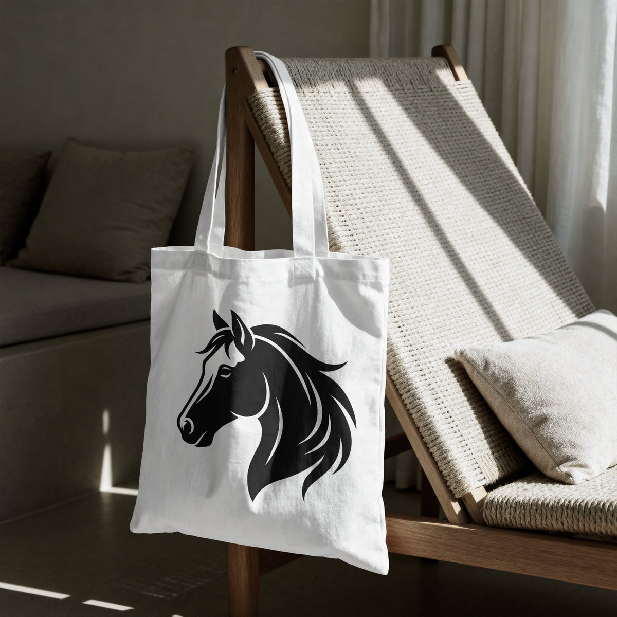 A white canvas tote bag with a black horse head graphic, hanging on a wooden lounge chair in a modern, sunlit living room.