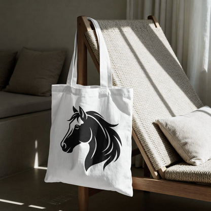 A white canvas tote bag with a black horse head graphic, hanging on a wooden lounge chair in a modern, sunlit living room.