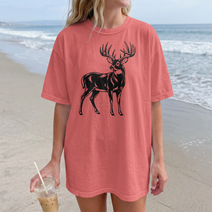 Person wearing a pink t-shirt with a black deer graphic on a beach.