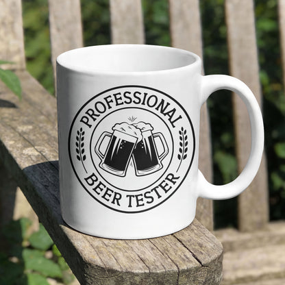 White mug with 'Professional Beer Tester' design on a wooden surface outdoors