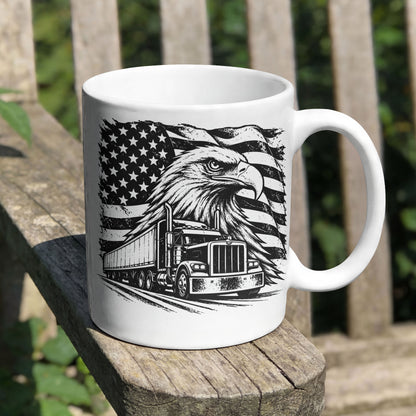 A white ceramic coffee mug with a black graphic print of an eagle head, a semi-truck, and a distressed American flag, sitting on a weathered wooden bench outdoors.