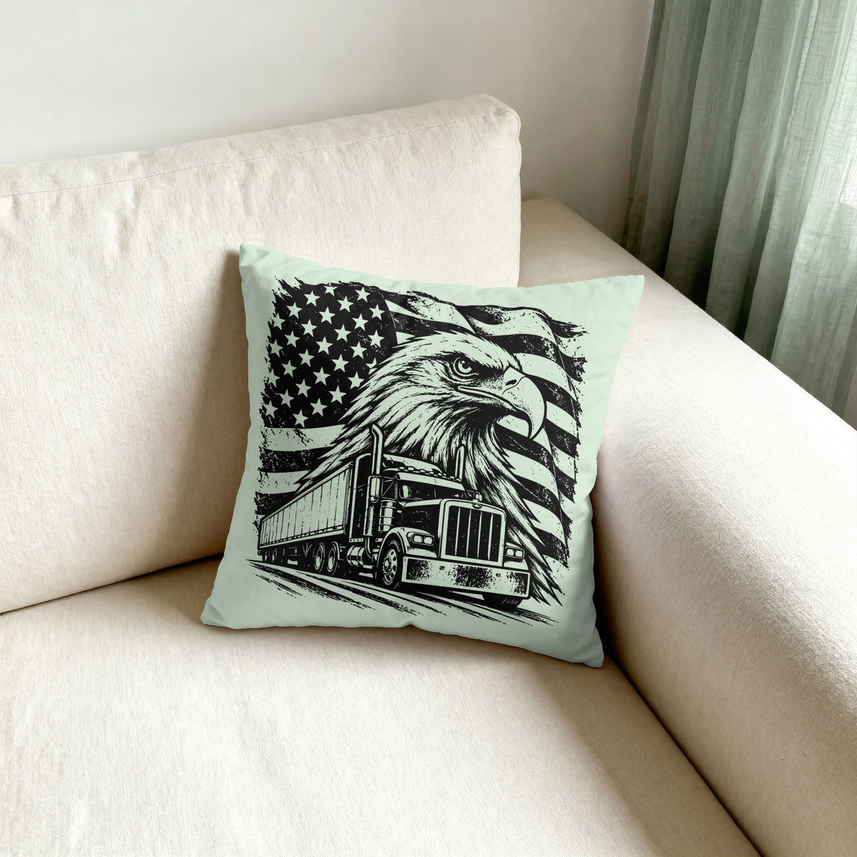 A square throw pillow with a black graphic print of an eagle head, an American flag, and a semi-truck on a light mint green background, resting on a cream-colored sofa.
