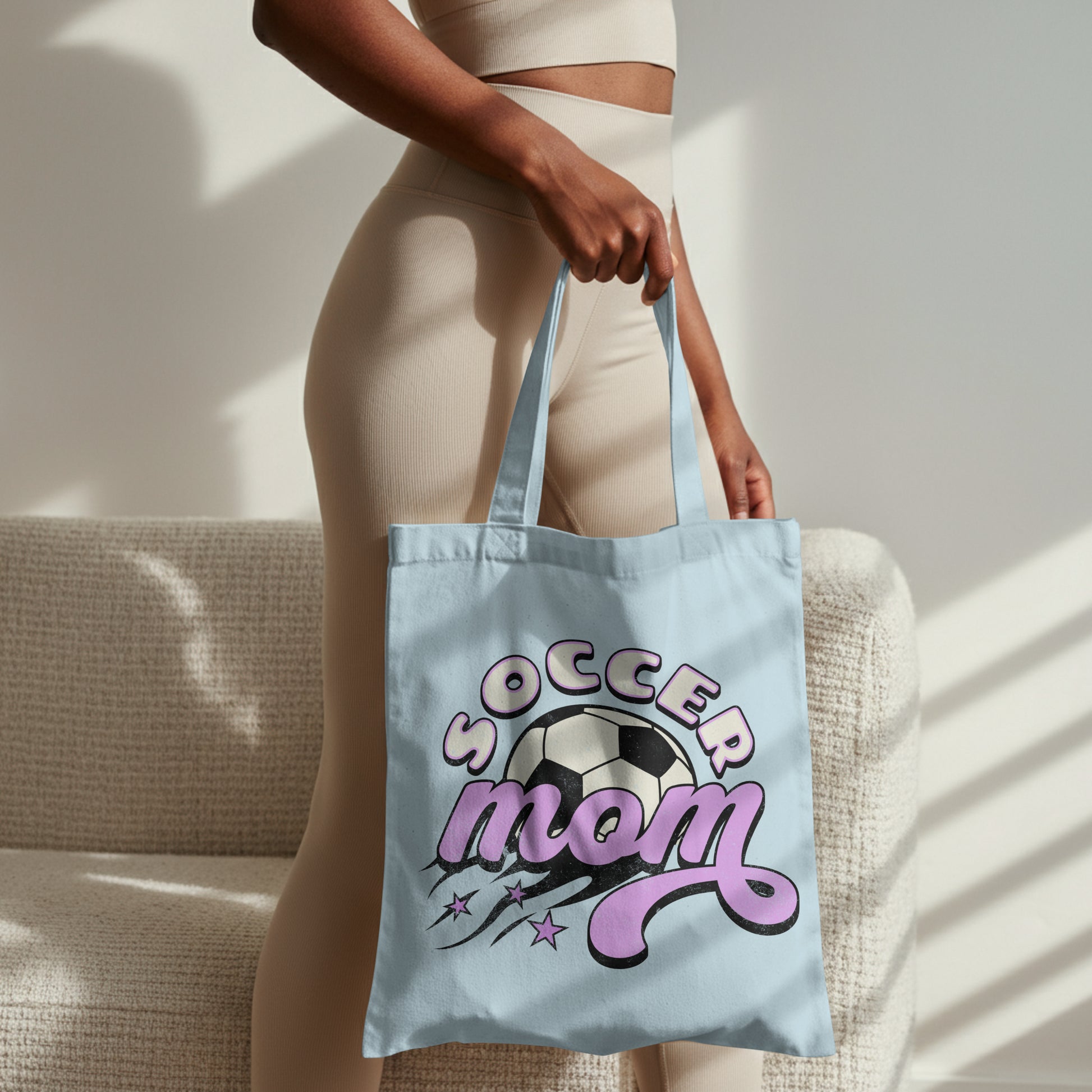 Person holding a light blue tote bag with 'Soccer Mom' design.